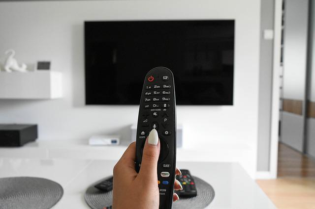 Hand mit TV-Fernbedienung vor Fernseher